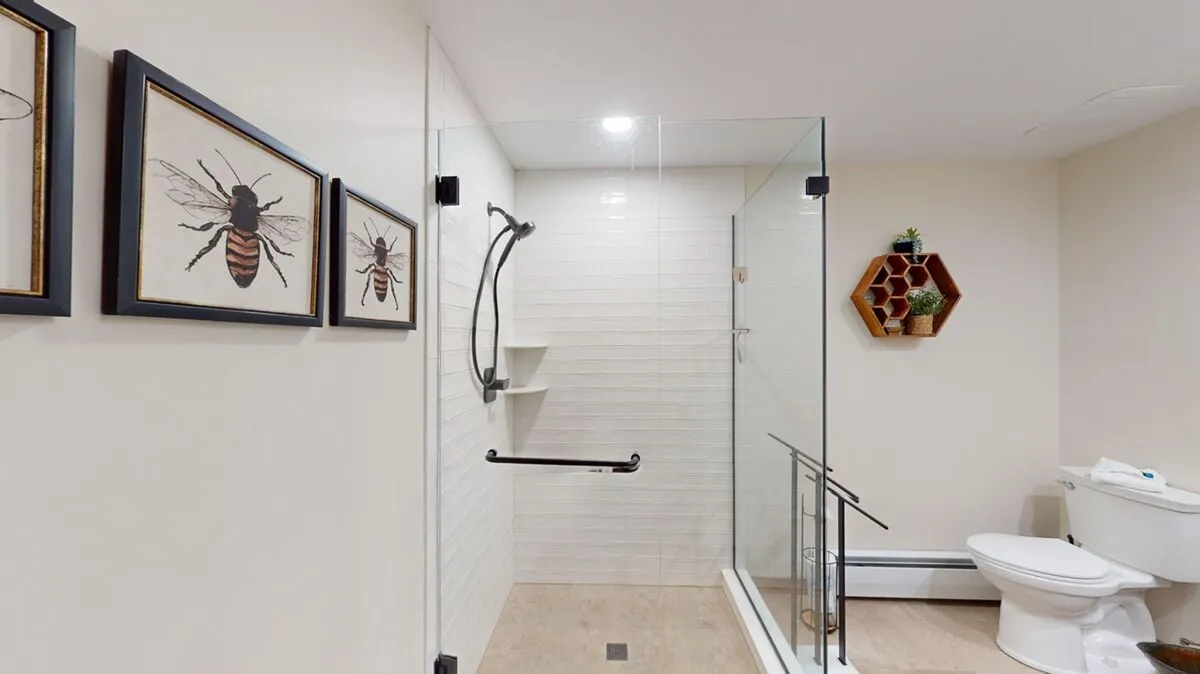 A tranquil ensuite bathroom with a glass-enclosed shower, bee-themed artwork, and a hexagonal shelf adorned with greenery. The room exudes freshness and relaxation, inviting guests to unwind and recharge.