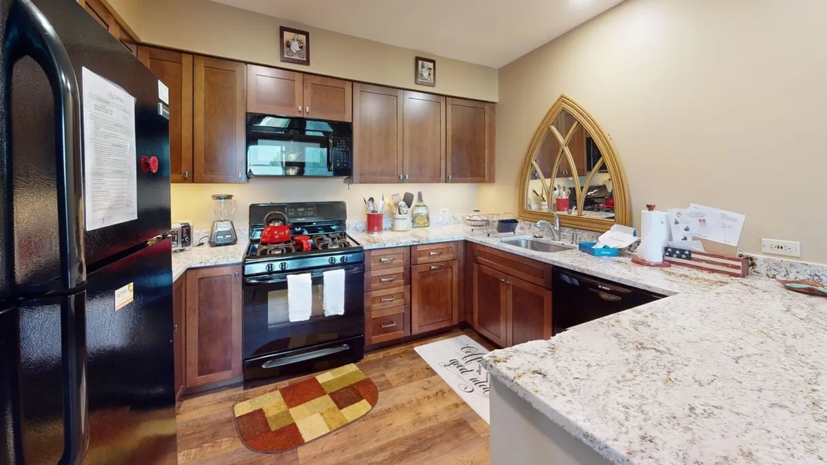 A cozy, inviting kitchen featuring sleek black and stainless steel appliances, granite countertops, and warm wood cabinetry. The layout is perfect for family meals or entertaining, with ample space to gather and share stories.