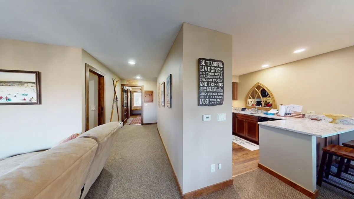 An inviting open-plan space that blends a comfortable sofa, a kitchen bar with seating, and stylish wall decor. The setup suggests a seamless connection between relaxing, cooking, and socializing, with the kitchen bar ideal for celebratory toasts or casual bites.
