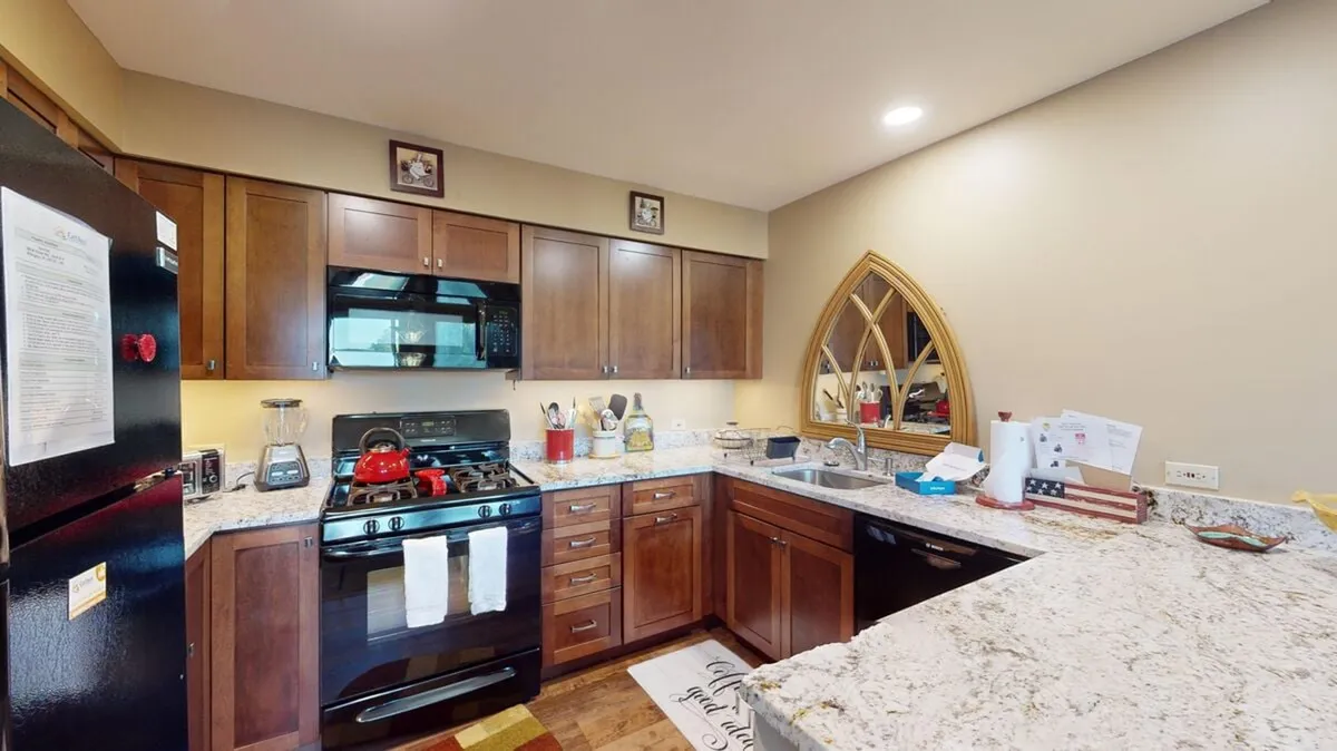 A modern kitchen with a large granite-topped island, a professional stove with a vibrant red kettle, and ample natural light pouring through an arched window. The space is equipped for both daily family use and festive entertaining, with appliances and seating for casual meals.