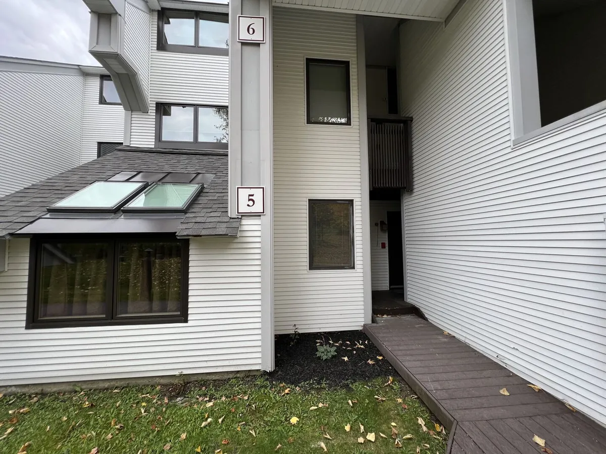 The image features the main entrance door of the townhome, accented by detailed windows and numbered signs. The outdoor area appears inviting and well-maintained, suggesting a welcoming transition from the wintry outdoors to the warmth inside.