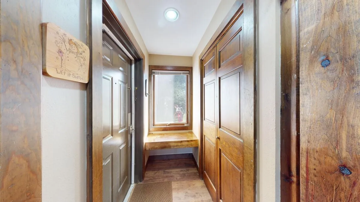 This image shows a welcoming entryway with wooden doors, a window streaming in natural light, and a wooden bench placed along the wall. The space feels bright and open, inviting guests to transition from indoors to the outdoors or vice versa.