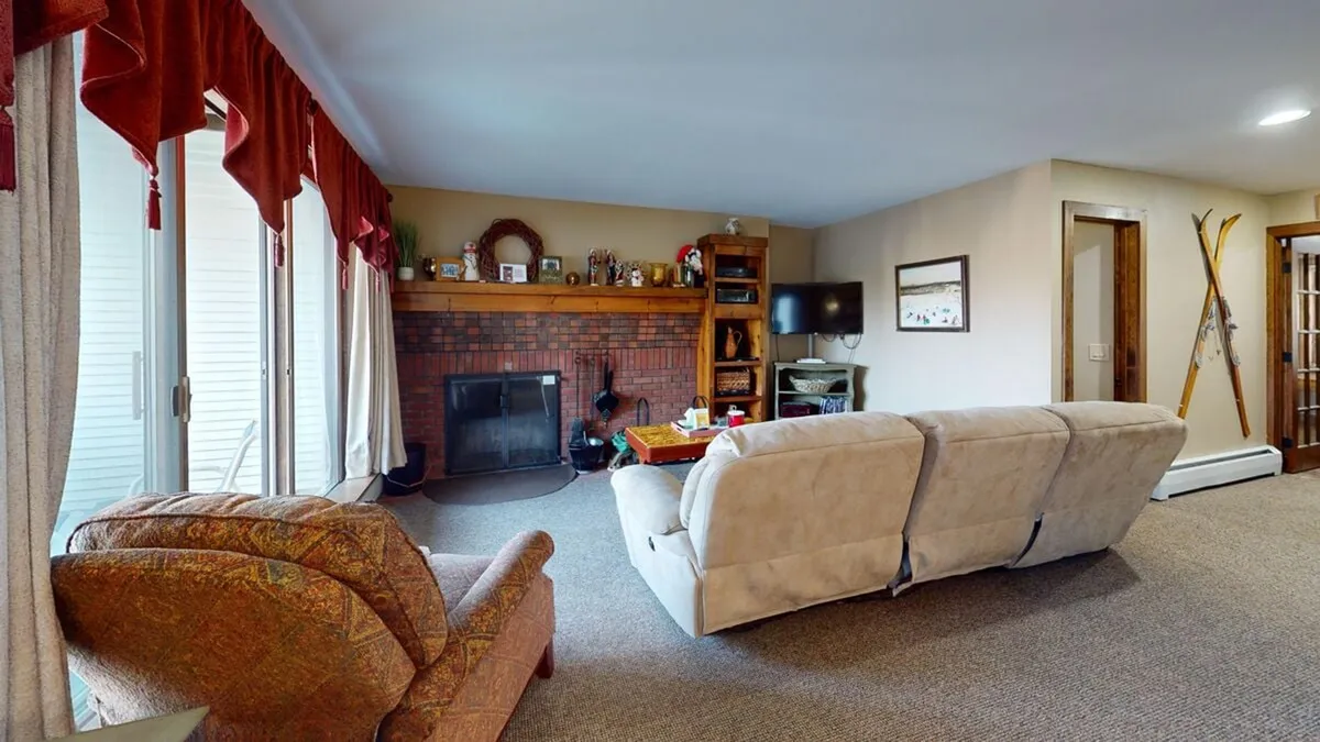 A cozy living room featuring a prominent stone fireplace flanked by built-in shelves, with a plush sectional sofa arranged to face the fire. Tasteful decorative elements line the shelves, and the space is bathed in warm, ambient lighting, inviting guests to gather and relax.