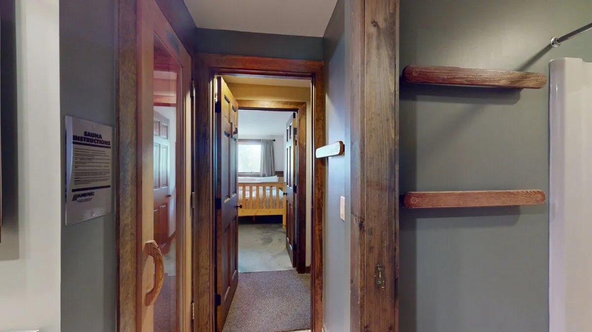 A cozy hallway with wooden doors leading to a bedroom, narrow carpeted floors, and built-in wall shelves. The hallway hints at the private, secluded nature of the suite and features visibility into the bedroom beyond.