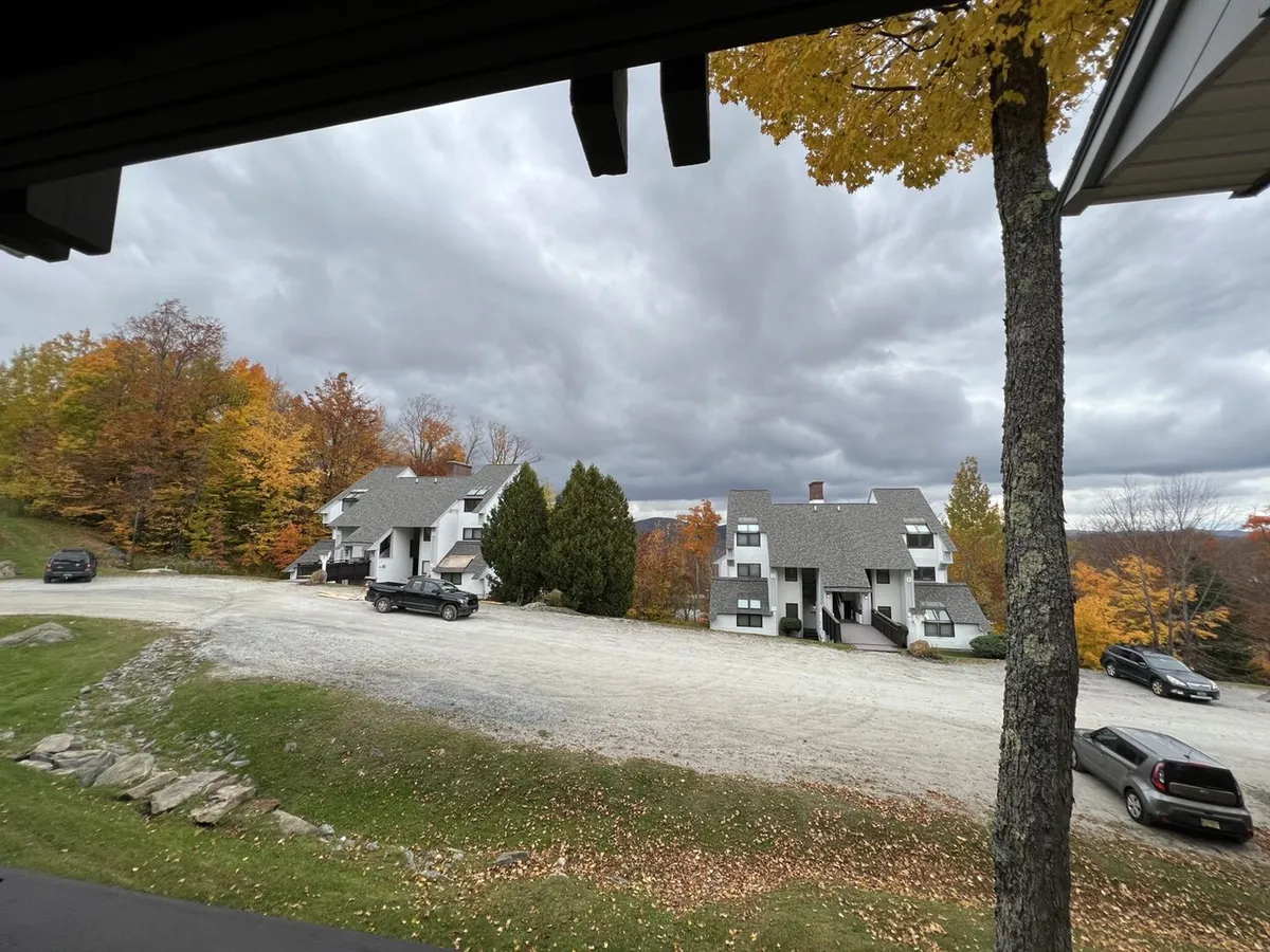 This exterior image captures the modern architecture of the Sunrise Village buildings surrounded by vibrant autumn foliage and a tranquil, cloudy sky. The scenic view includes hints of nature trails and the inviting proximity to outdoor adventure.