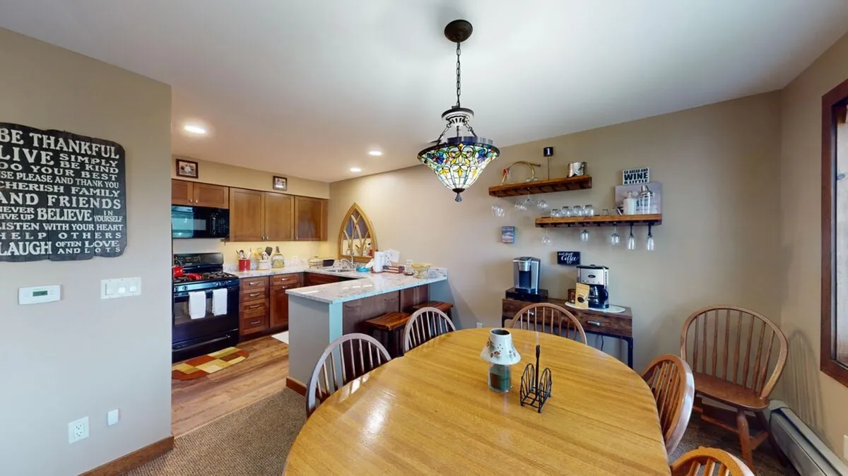 This image showcases a warm, inviting dining area featuring a large dining table, a striking stained glass chandelier, a kitchen island, and decorative wall art. The overall ambiance is lively yet cozy, ideal for group meals and entertaining guests.