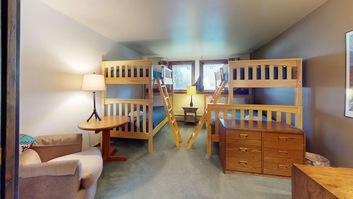 This image features a cozy bedroom with multiple bunk beds, an armchair, a lamp, and a nightstand. The arrangement evokes a family-friendly, camp-like atmosphere, perfect for group or sibling sleepovers after outdoor adventures.