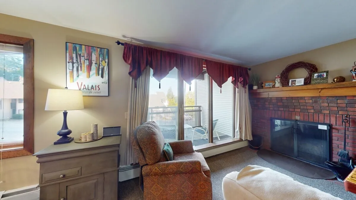 A cozy, inviting living room interior with a fireplace, comfortable armchair, and a large window offering mountain views. The setting suggests relaxation after a day of adventure, connecting interior comfort with the surrounding landscape.